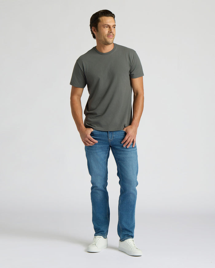 Man wearing a gray t-shirt and blue jeans on a white background. MODEL_INFO: Model is 6'0" wearing size L short