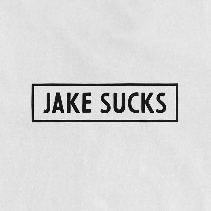 White vintage T-shirt with black text inside a rectangular border that reads "JAKE SUCKS" in bold, uppercase letters.