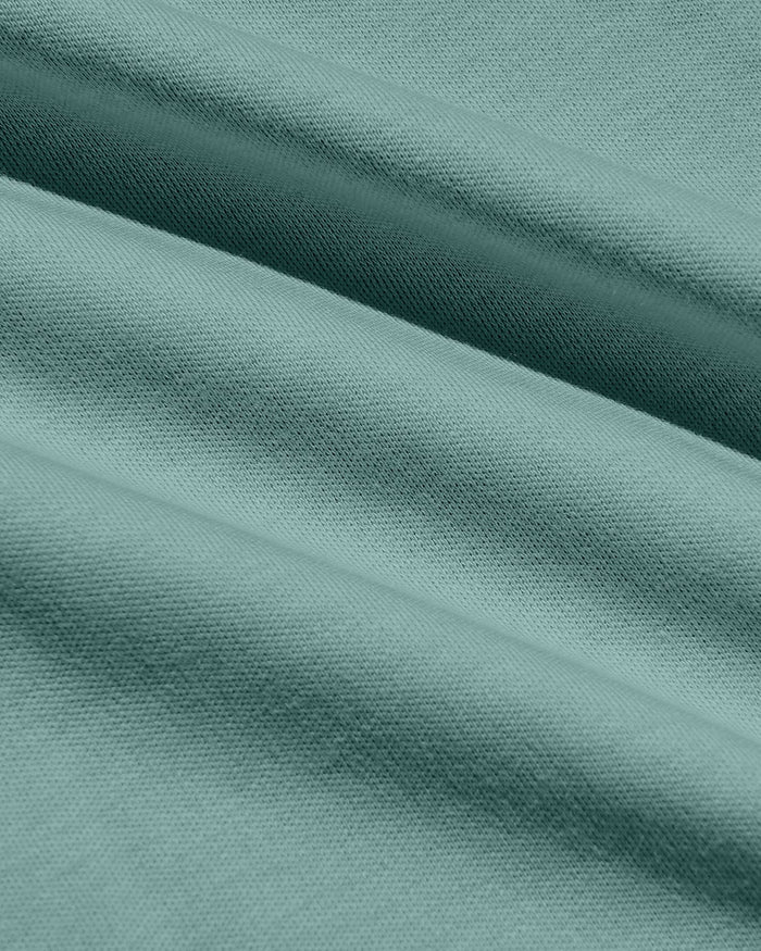 A close-up of draped fabric in a muted sage green color, showing the texture and weave with soft folds.