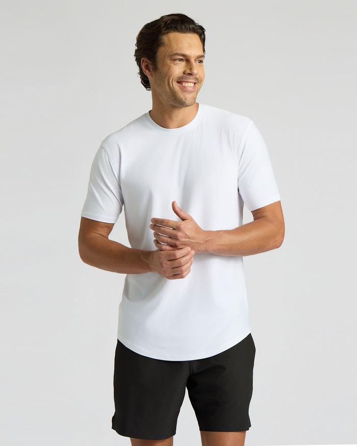 A smiling man wearing a white Active Curved Hem Crew Tee - Men's Moisture Wicking Performance T-Shirt paired with black shorts, showcasing a casual and comfortable men's basics look.