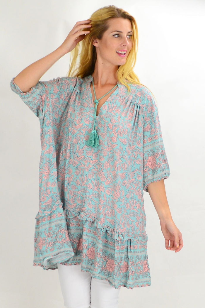 Aqua blue Style Fashion ruffle tunic top with flowy fabric and decorative ruffles at the hem, displayed on a hanger.