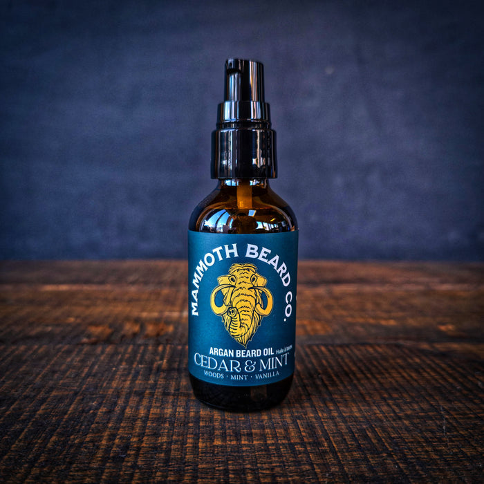 Close-up of Mammoth Beard Co Cedar & Mint Argan Beard Oil pump bottle on dark wooden surface, premium natural beard oil for hydration and shine.