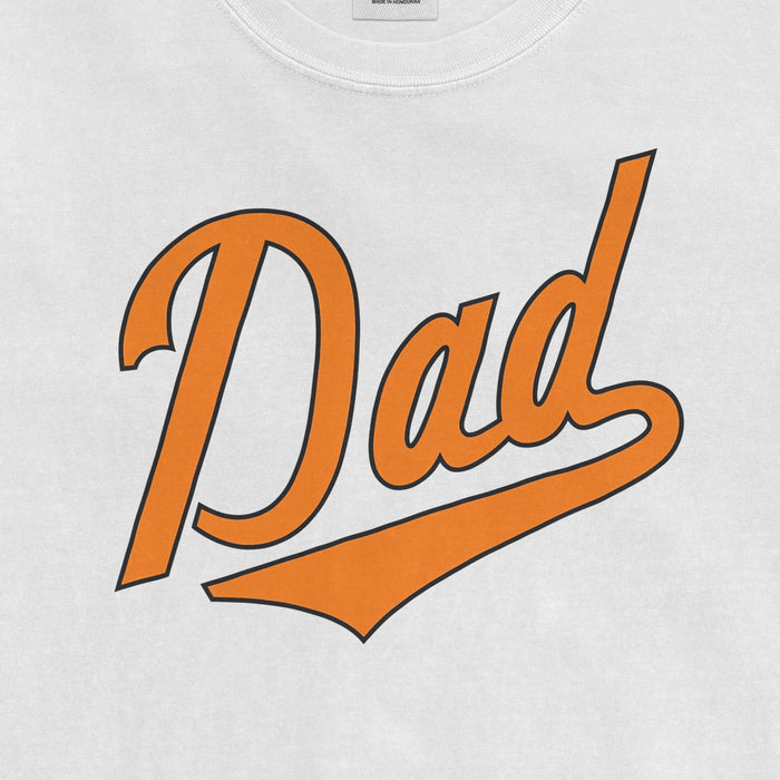 White Comfort Colors T-shirt with "Baltimore Dad" in orange and black script font, designed for baseball dads.