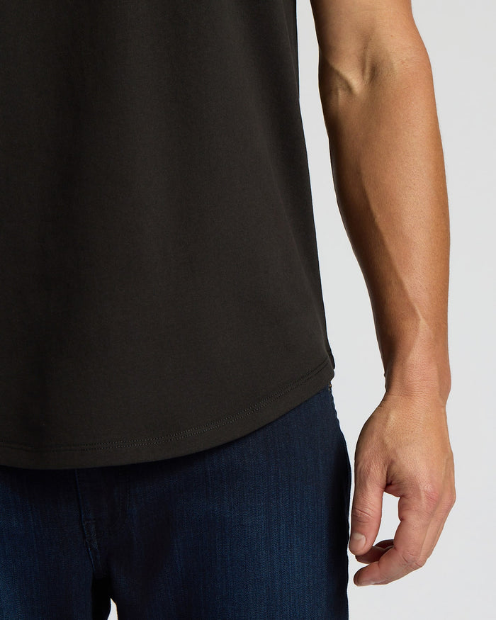 Close-up of a man wearing an All Black Heavyweight Curved Hem Crew 6-Pack shirt paired with dark blue jeans, highlighting the curved hem detail on the black heavyweight fabric.
