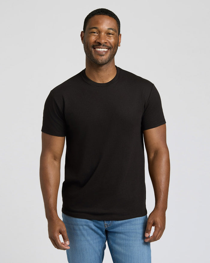 Man wearing a black t-shirt and blue jeans against a plain background