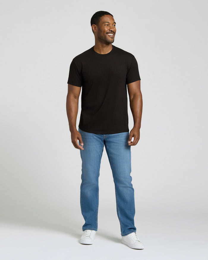 Man wearing a black t-shirt, blue jeans, and white sneakers on a plain background. MODEL_INFO: Model is 5'8" wearing size M short