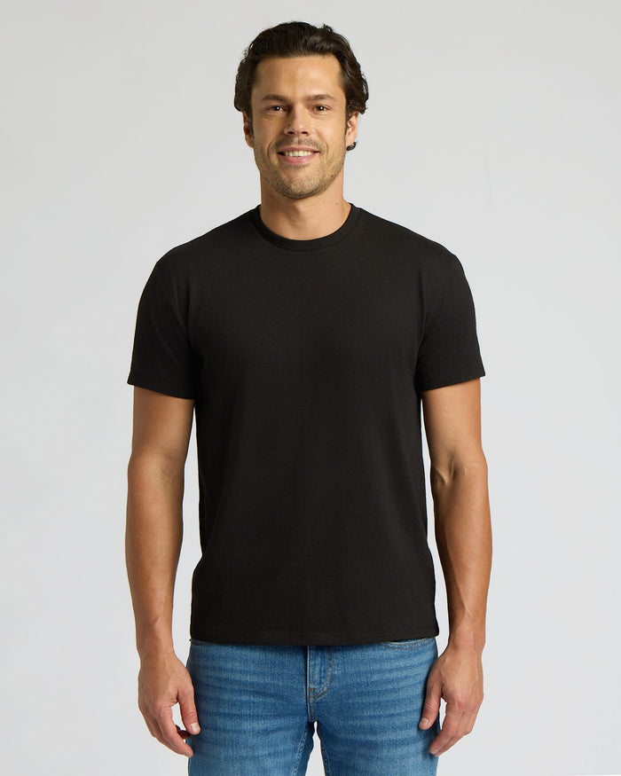 Man wearing a black t-shirt and blue jeans on a gray background