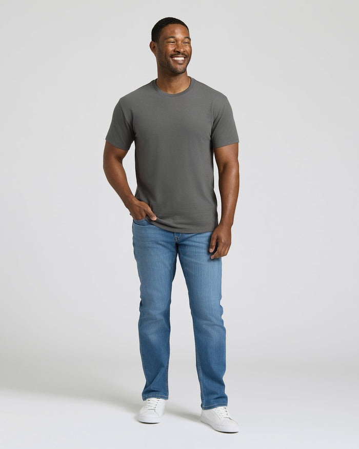 Man wearing a gray t-shirt and blue jeans standing against a plain background. MODEL_INFO: Model is 5'8" wearing size M short