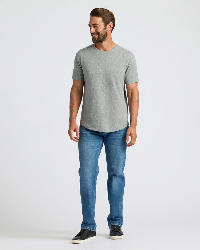 Man wearing Heather Gray Curved Hem Classic Crew Neck, blue jeans, and black sneakers.