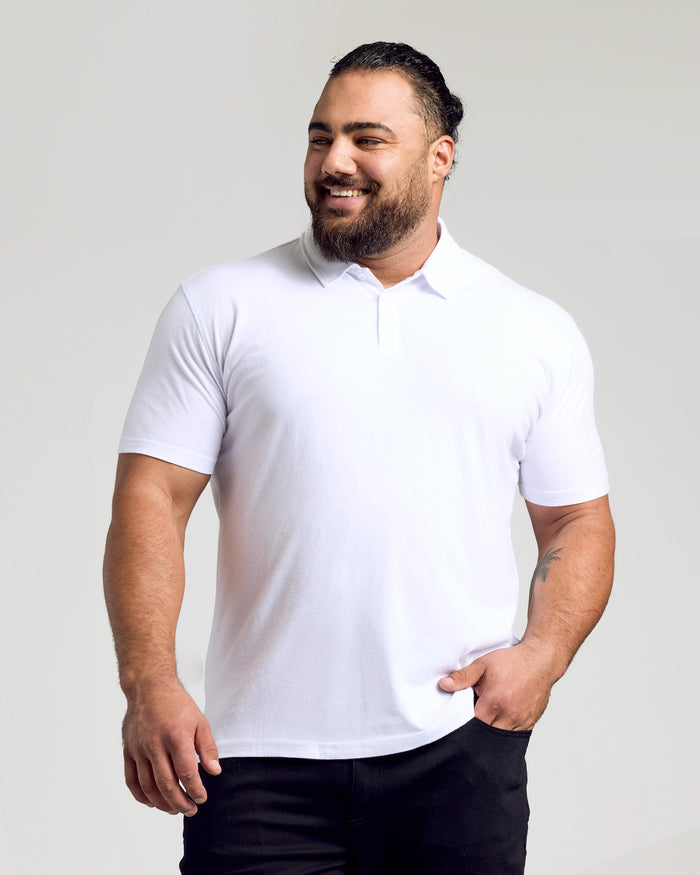 Man wearing White Classic Polo, smiling with hand in pocket.