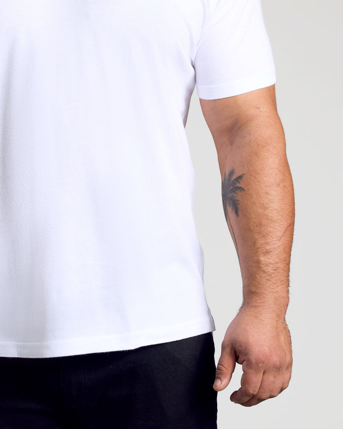 White Classic Polo worn by person with palm tree tattoo visible on forearm.