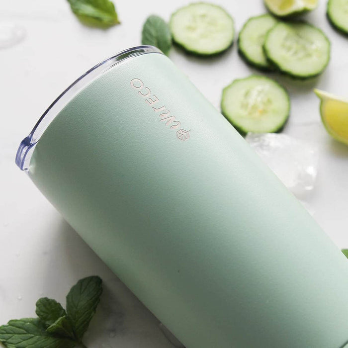 Sage insulated tumbler laid on its side on a white surface with sliced cucumber, lime, mint & ice cubes.