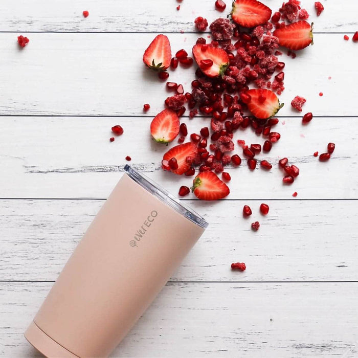 Ever Eco light pink insulated tumbler laid on its side on a white wooden surface with sliced strawberries, pomegranate & frozen raspberries artistically placed to look as though they're spilling out.