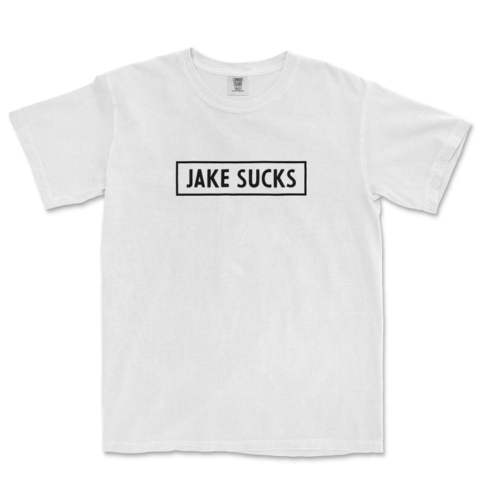 White Comfort Colors® vintage T-shirt with bold black text inside a rectangle that reads "JAKE SUCKS" on the front.