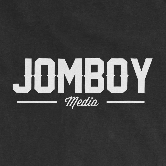 Black Comfort Colors T-shirt featuring a white "Jomboy Media" logo with bold uppercase text and a cursive "Media" underneath.