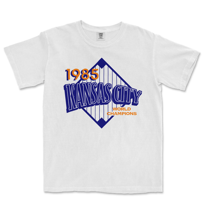 White Comfort Colors T-shirt featuring a vintage Kansas City 1985 World Champions graphic in blue and orange.