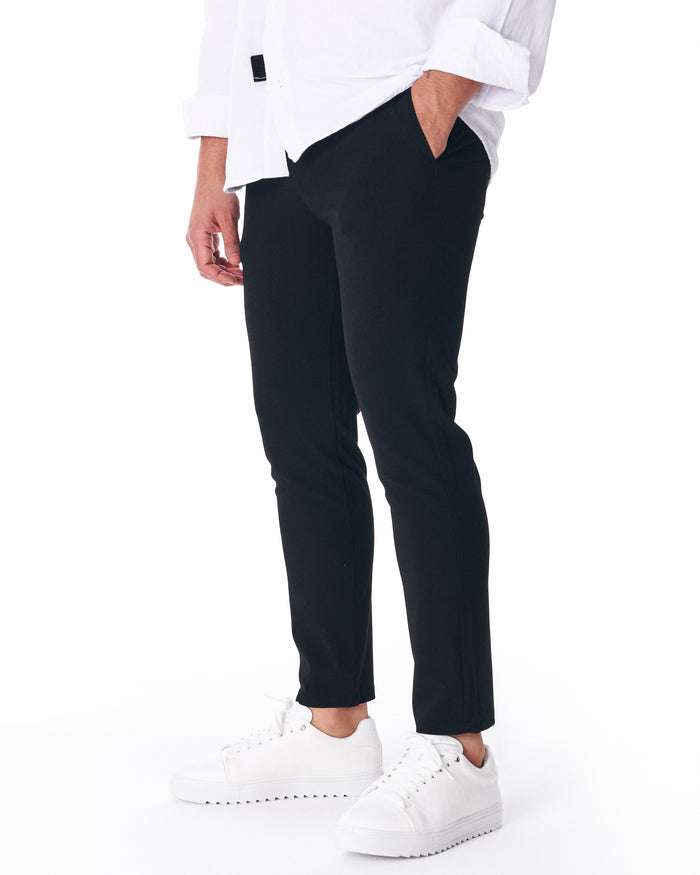 Martin Valen men's black trousers, close-up of leg with white sneakers and cropped hem above the ankle