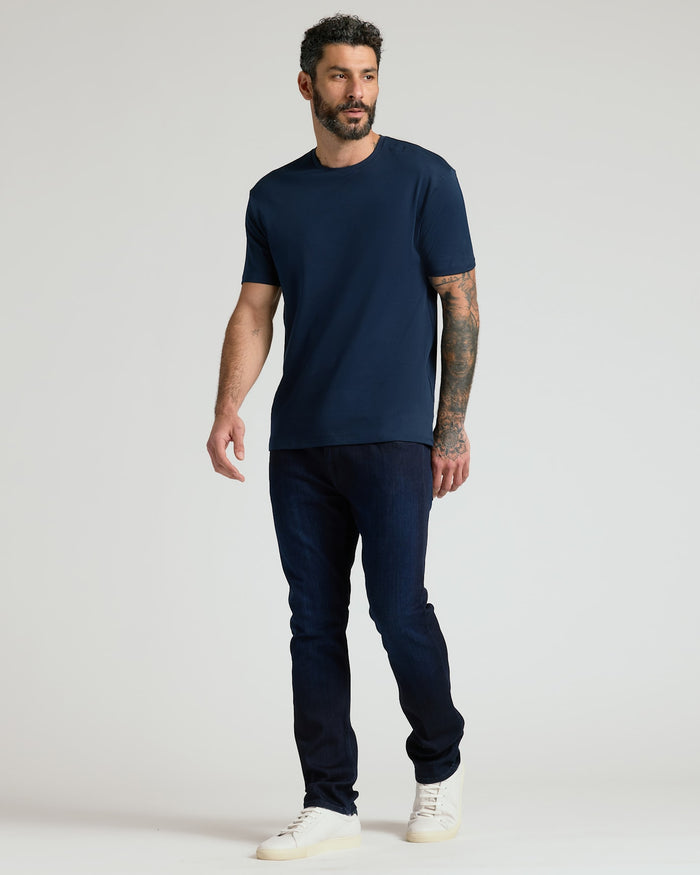 Man wearing a navy crew neck t-shirt from the Pima Cotton Blend Crew 4-Pack, paired with dark jeans and white sneakers, standing against a light background in a casual pose