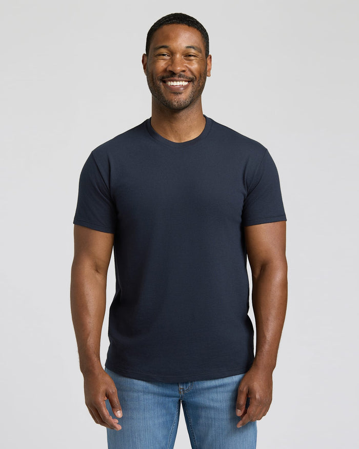 Man wearing a navy blue t-shirt and blue jeans against a plain background.
