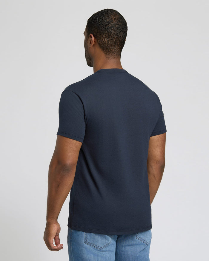 Man wearing a navy blue t-shirt and light blue jeans on a plain background