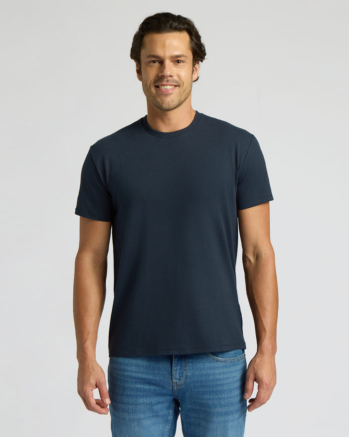 Man wearing a navy blue t-shirt and blue jeans on a light gray background