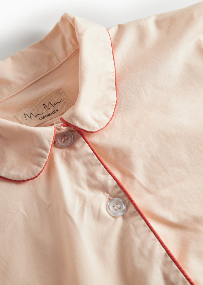 Detalje af beige pyjamas: ståkrave med orange kant og knaplukning ved halsen