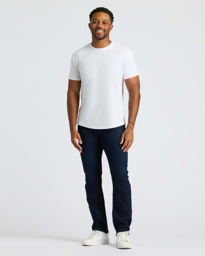 Man wearing All White Curved Hem Classic Crew Neck T-shirt, smiling, relaxed pose.