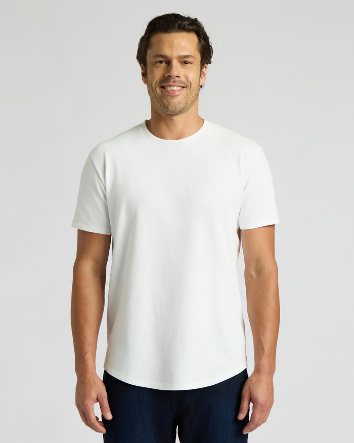 Man wearing a white Heavyweight Curved Hem Crew 6-Pack t-shirt, standing and smiling with a clean, minimal background, showcasing a classic men's basics style.