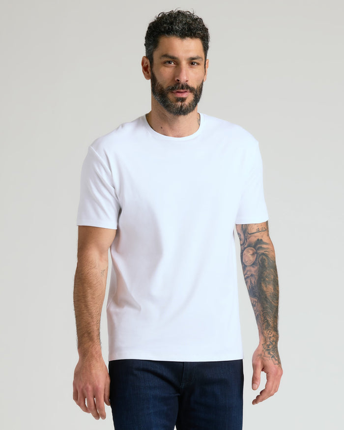 Man wearing a plain white crew neck t-shirt standing against a neutral background, showcasing the Pima Cotton Blend Crew 4-Pack as a comfortable men's basics essential.