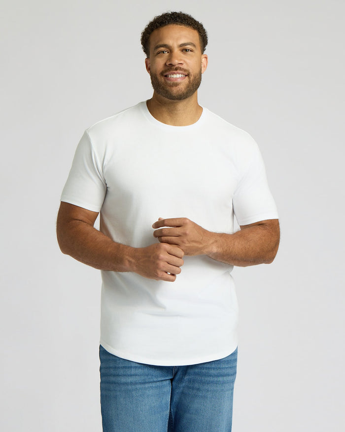 Smiling man wearing an All White Tall Heavyweight Curved Hem Crew 3-Pack t-shirt paired with blue jeans, showcasing a classic men's basics style.