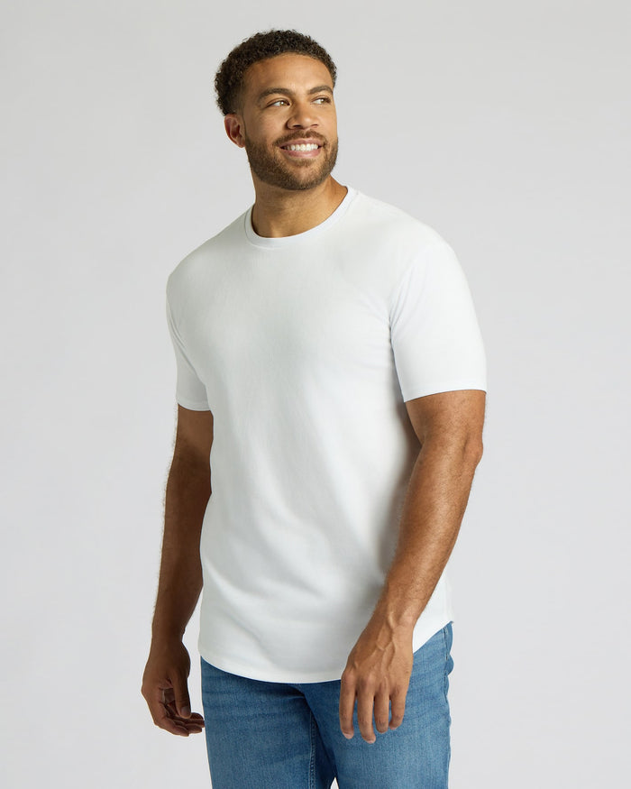 Smiling man wearing a white Tall Heavyweight Curved Hem Crew 3-Pack t-shirt paired with blue jeans, showcasing a classic men's basics style from True Classic.